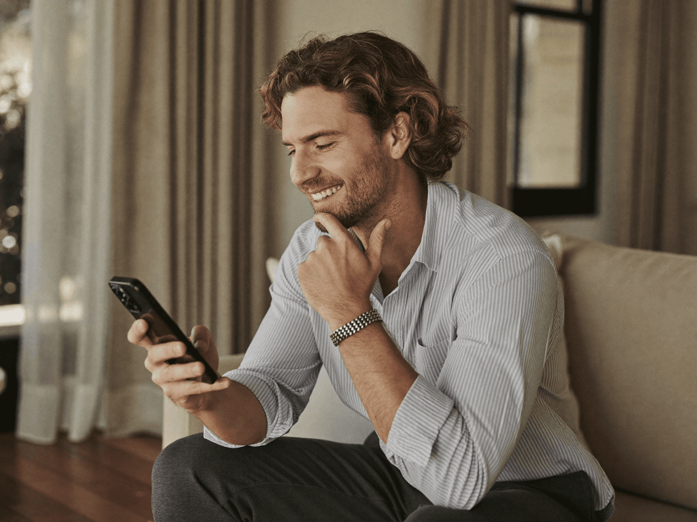 A relaxed man smiling at his phone on the sofa at home